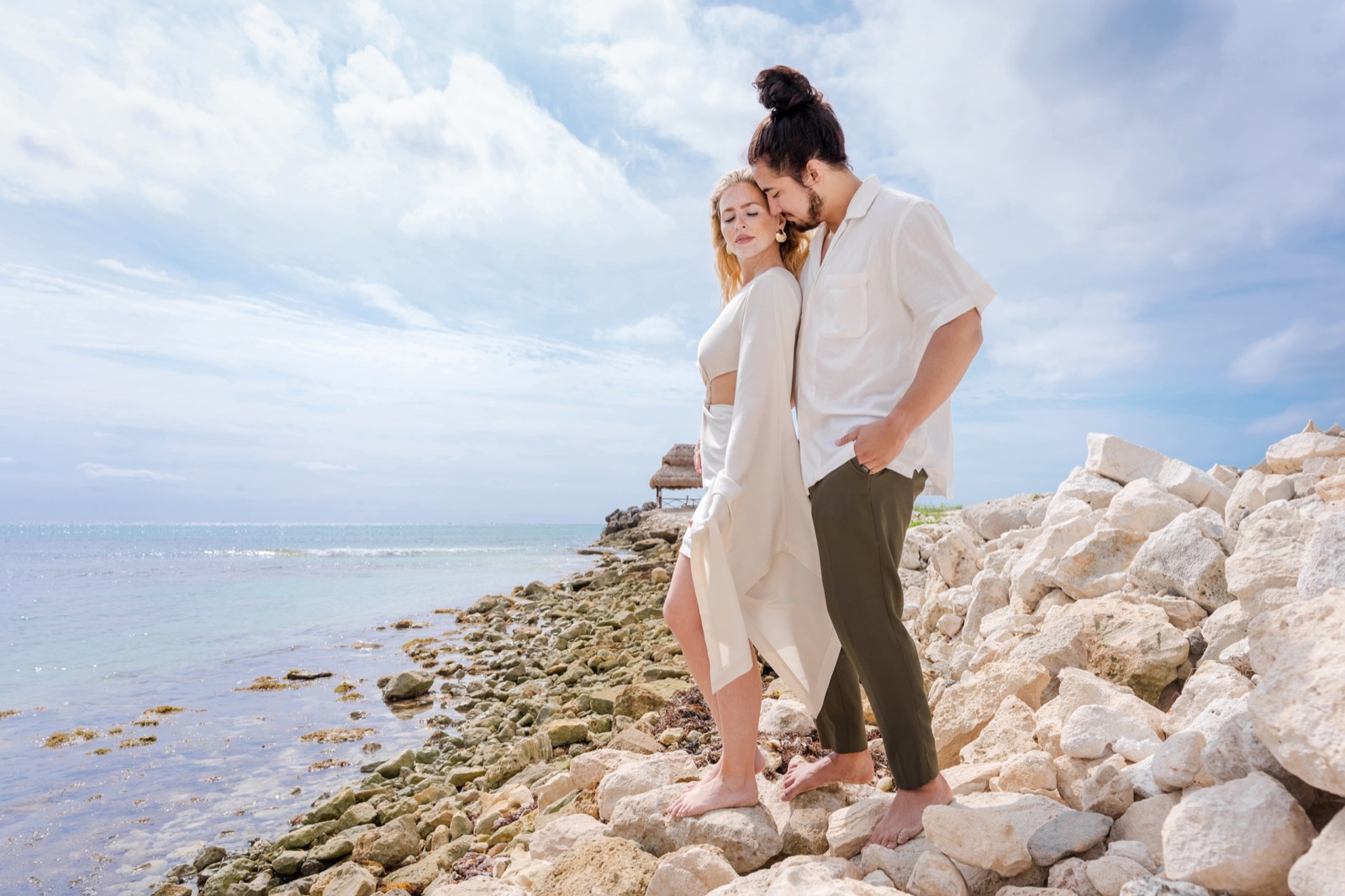 Newly engaged couple laughing together in warm low light on the sand shortly after the proposal, ring visible on her hand