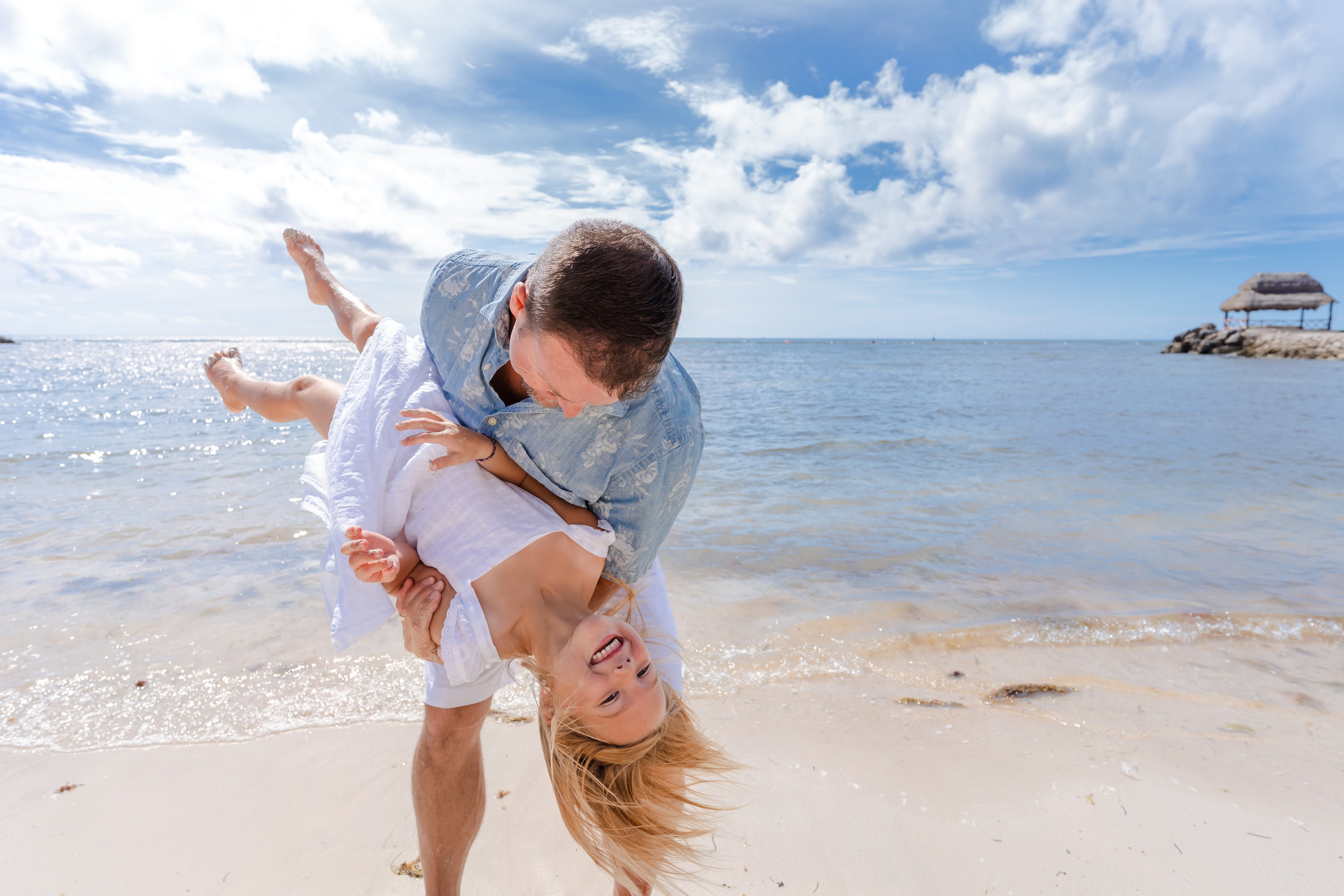A family laughs together as the wind catches their linens at golden hour in Cancún, photographed by IVAE Studios.