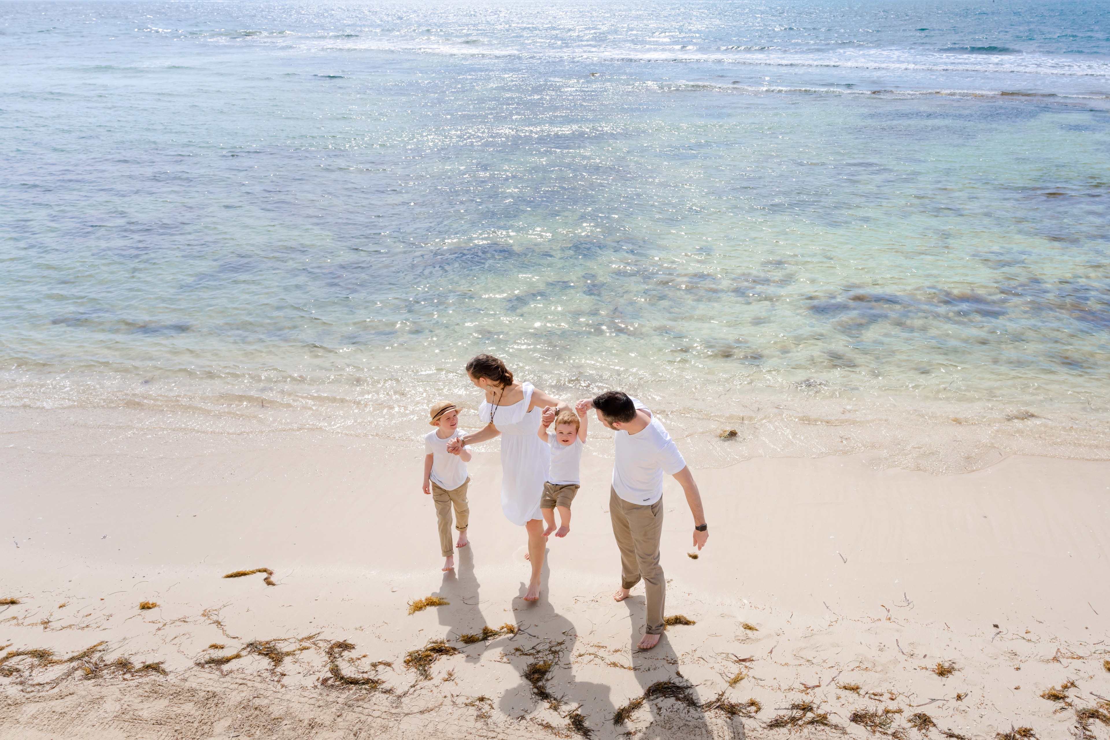 Multigenerational family walking a quiet, empty stretch of Caribbean sand at golden hour during an IVAE Studios family photo session near Cancun, Mexico