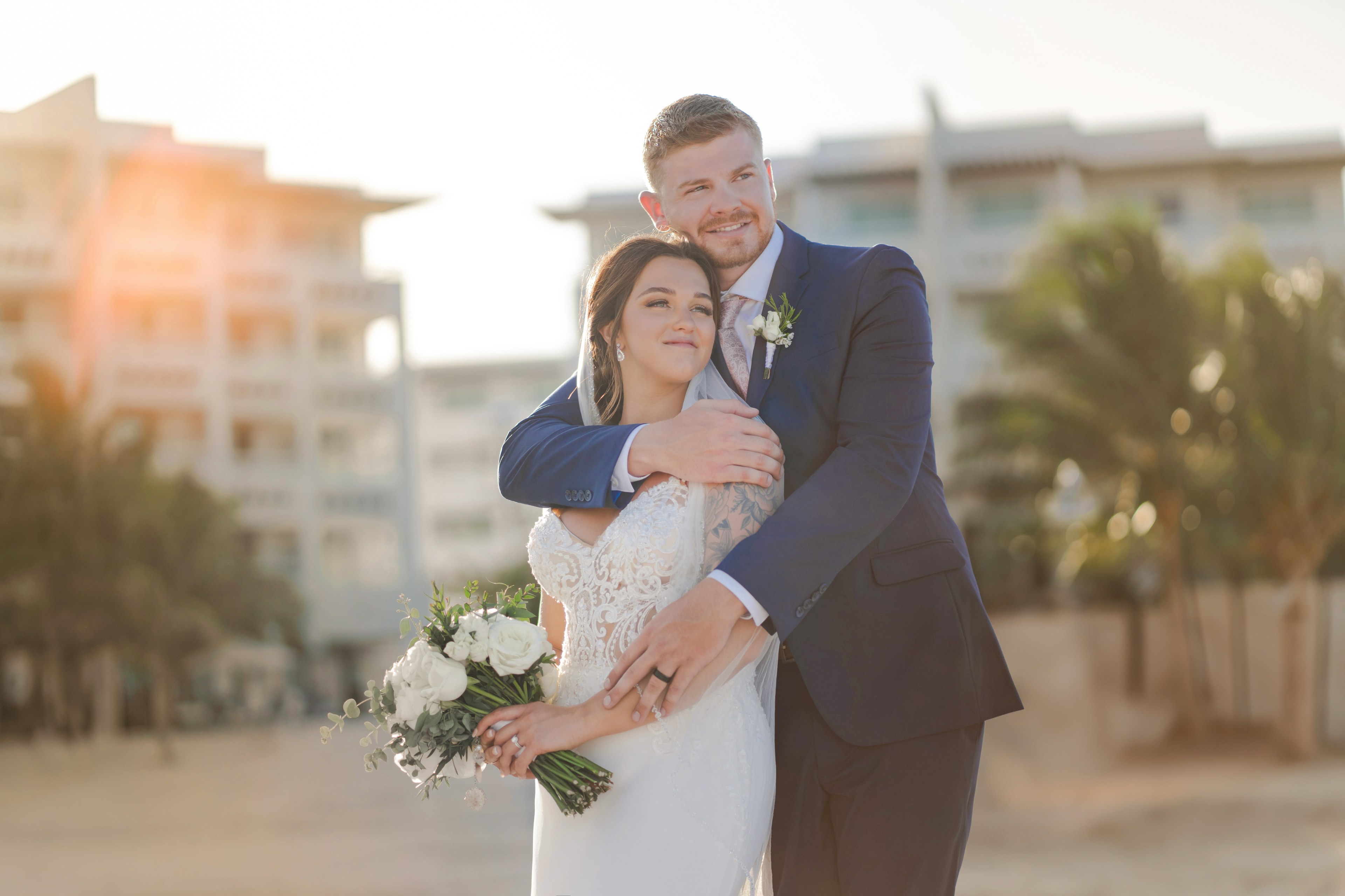 A couple reviewing wedding plans on a video call, with IVAE Studios golden-hour editorial photography of a Cancun beach ceremony in the background, Mexico destination wedding planning